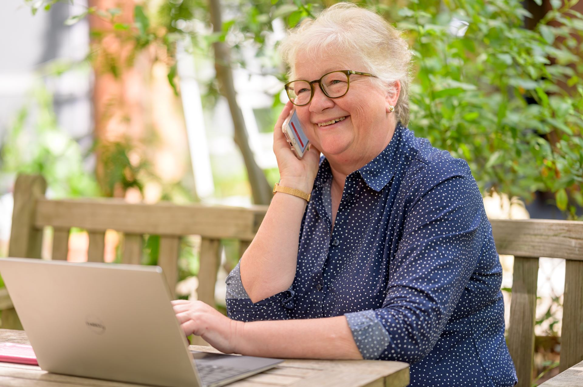 A woman on a bench outside speaking into a mobile phone